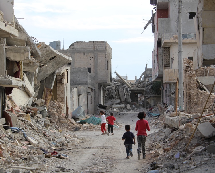 Children walk through streets filled with rubble and destroyed buildings either side